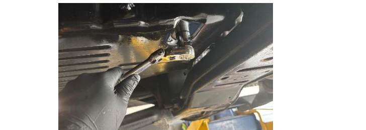 Removing the transmission pan drain plug with a 3/4 inch wrench to drain the fluid
